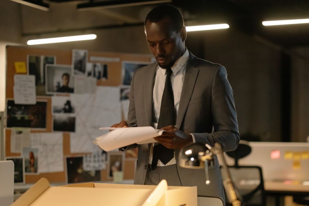 An African American detective reviews documents in a modern office setting, focusing on evidence files.